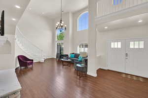 Entryway with a towering ceiling, wood finished floors, stairway, a chandelier, and baseboards