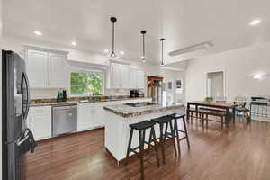Kitchen featuring black appliances, light stone counters, white cabinetry, dark wood-type flooring, and a kitchen island
