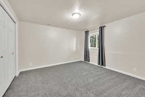Unfurnished bedroom with a textured ceiling, carpet, a closet, and baseboards