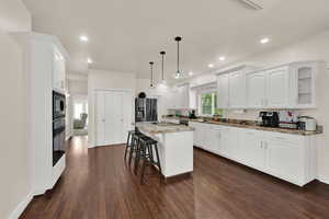 Kitchen with stainless steel fridge with ice dispenser, a breakfast bar area, dark wood finished floors, white cabinets, and light stone countertops