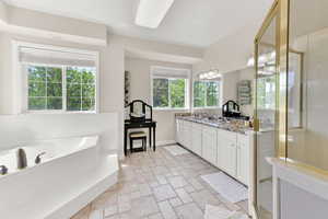 Full bath with vanity, stone finish flooring, a garden tub, a stall shower, and baseboards