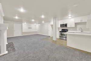 Kitchen with appliances with stainless steel finishes, light colored carpet, a sink, white cabinets, and light countertops