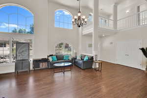 Living room with a high ceiling, dark wood-style flooring, a chandelier, and baseboards