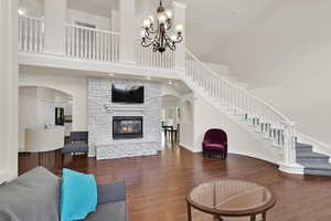 Living room featuring wood finished floors, a towering ceiling, stairs, a fireplace, and baseboards