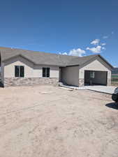View of front of property featuring roof with shingles, stone siding, and a garage