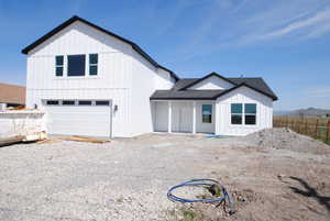View of front of house featuring board and batten siding, a shingled roof, fence, gravel driveway, and an attached garage.  Front yard is fully grassed.