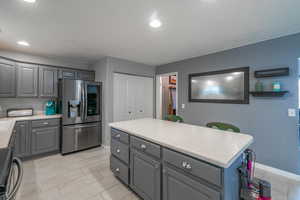 Kitchen featuring stainless steel fridge with ice dispenser, gray cabinets, range, light countertops, and baseboards