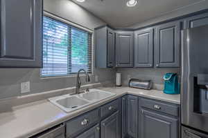 Kitchen featuring stainless steel fridge with ice dispenser, a sink, gray cabinets, light countertops, and dishwasher