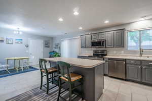 Kitchen with appliances with stainless steel finishes, gray cabinets, a sink, a breakfast bar area, and a center island