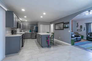 Kitchen with black appliances, gray cabinetry, arched walkways, light countertops, and recessed lighting