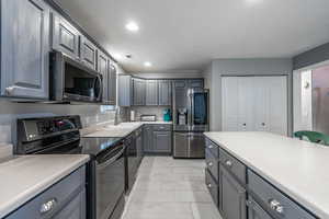 Kitchen featuring stainless steel appliances, gray cabinetry, a sink, recessed lighting, and light countertops