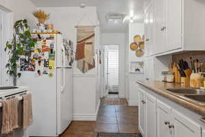 Kitchen with white appliances, white cabinetry, a sink, dark tile patterned flooring, and baseboards