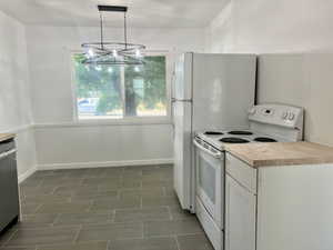 Kitchen with white range with electric cooktop, baseboards, a chandelier, white cabinets, and decorative light fixtures