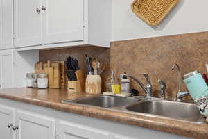 Kitchen view of white cabinetry, backsplash, a sink, and dark countertops