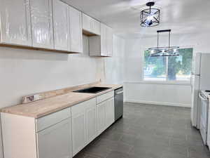 Kitchen with stainless steel dishwasher, white range with electric stovetop, white cabinets, light countertops, and baseboards