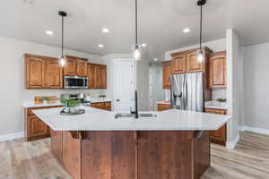 Kitchen featuring stainless steel appliances, a sink, baseboards, light countertops, and light wood-style flooring