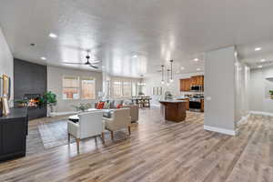 Living room featuring a large fireplace, baseboards, light wood-style flooring, recessed lighting, and ceiling fan