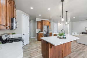 Kitchen with appliances with stainless steel finishes, open floor plan, brown cabinetry, light countertops, and light wood-type flooring