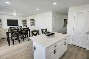 Kitchen with light wood finished floors, a center island, white cabinets, open floor plan, and recessed lighting