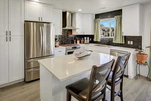 Kitchen featuring appliances with stainless steel finishes, wall chimney range hood, a sink, light wood-type flooring, and recessed lighting