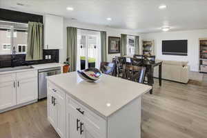 Kitchen featuring dishwasher, a sink, light wood-style flooring, a kitchen island, and decorative backsplash