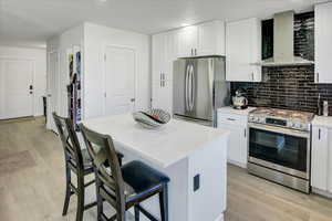 Kitchen featuring appliances with stainless steel finishes, wall chimney range hood, light wood-type flooring, backsplash, and recessed lighting