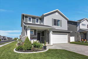 View of front of home featuring concrete driveway, stone siding, an attached garage, and a front lawn