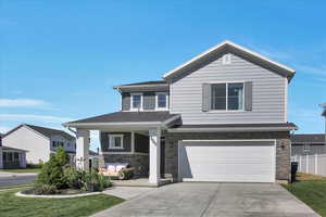 View of front of property with stone siding, driveway, an attached garage, and fence