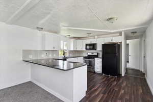 Kitchen with black appliances, a peninsula, white cabinetry, baseboards, and a textured ceiling