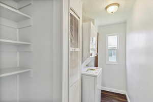 Laundry room with stacked washer / dryer, dark wood finished floors, a heating unit, baseboards, and a textured ceiling
