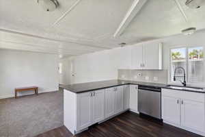 Kitchen featuring dishwasher, a textured ceiling, a sink, a peninsula, and white cabinetry