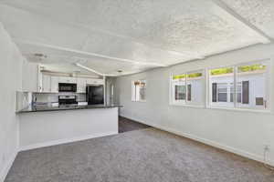 Kitchen featuring black appliances, dark carpet, white cabinetry, baseboards, and a textured ceiling
