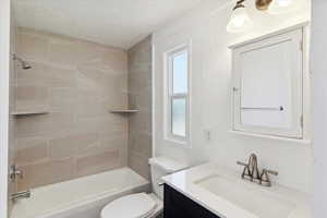 Bathroom with a textured ceiling, toilet, vanity, and tub / shower combination