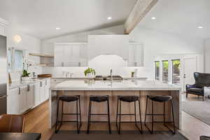 Kitchen with open shelves, white cabinetry, a kitchen breakfast bar, a center island with sink, and beamed ceiling