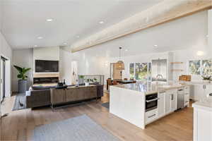 Kitchen featuring lofted ceiling, white cabinets, appliances with stainless steel finishes, an island with sink, and plenty of natural light