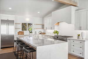 Kitchen with high end appliances, open shelves, a sink, lofted ceiling, and light wood-style floors