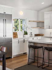 Kitchen with high quality fridge, a kitchen bar, white cabinetry, light countertops, and wood finished floors