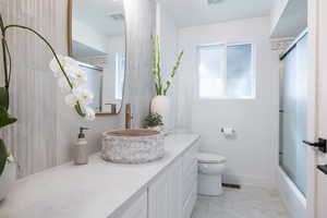 Bathroom with toilet, vanity, tile patterned floors, shower / bath combination with glass door, and baseboards
