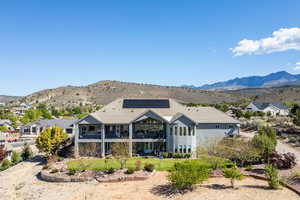 Rear view of house with a mountain view, roof mounted solar panels, a balcony, and a yard