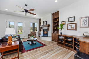 Living area with a lit fireplace, a ceiling fan, recessed lighting, french doors, and light wood-style flooring