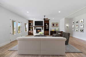 Living room featuring recessed lighting, light wood-style floors, a glass covered fireplace, built in shelves, and ceiling fan