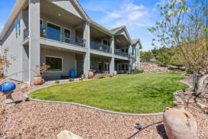 Rear view of house featuring stucco siding, a balcony, and a lawn