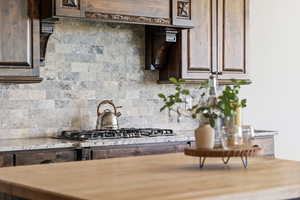 Kitchen with backsplash, light stone countertops, and dark brown cabinets