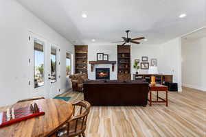 Living area featuring a glass covered fireplace, baseboards, recessed lighting, ceiling fan, and light wood-type flooring