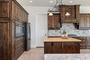 Kitchen with dark brown cabinets, decorative backsplash, a center island, pendant lighting, and stainless steel fridge