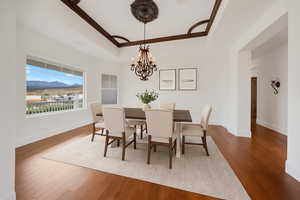 Dining area featuring a raised ceiling, wood finished floors, a mountain view, a chandelier, and ornamental molding