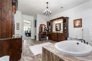Ensuite bathroom with vanity, a jetted tub, a chandelier, and marble finish flooring