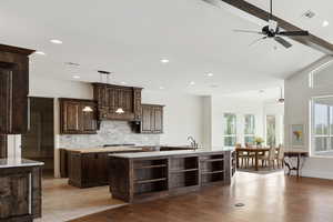 Kitchen featuring beam ceiling, dark brown cabinetry, backsplash, light stone counters, and recessed lighting