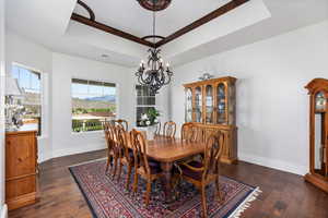 Dining area featuring a raised ceiling, ornamental molding, a chandelier, wood-type flooring, and baseboards