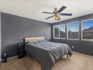 Carpeted bedroom with ceiling fan, baseboards, and a textured ceiling